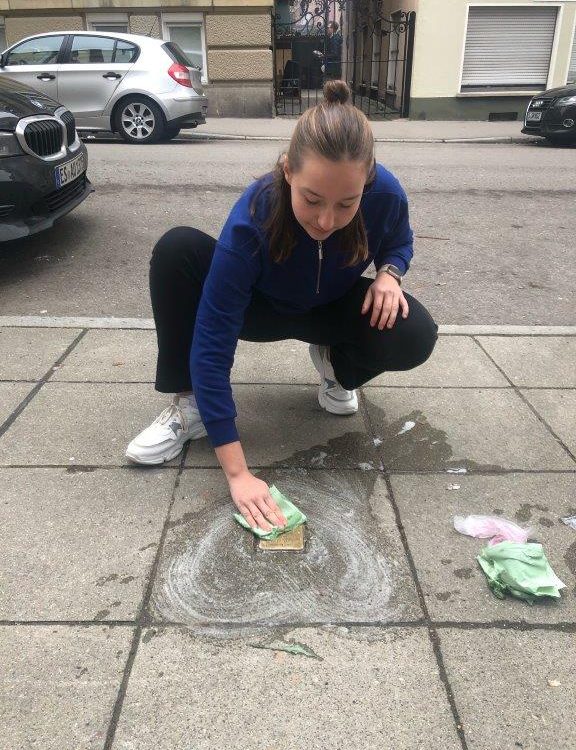 Schülerinn reinigt Stolperstein