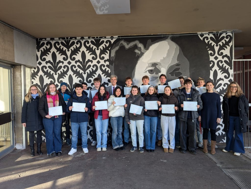 PXL_20250114_122159378.MP_-1024x771 Schüler stehen vor einer Wand und halten ihre DELF Zertifikate